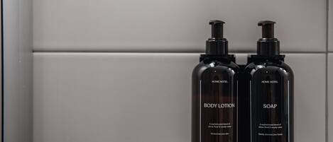 Dos botellas negras con etiquetas que dicen "BODY LOTION" y "SOAP", con dosificador, sobre una superficie blanca.