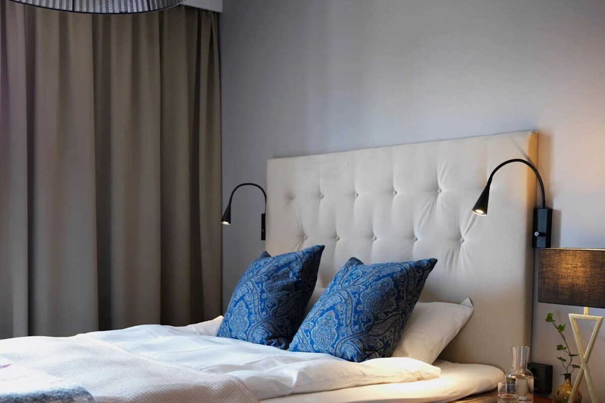 Un dormitorio ordenado con un cabecero capitonado, una cama con almohadas de estampado azul, una lámpara de noche y una silla.