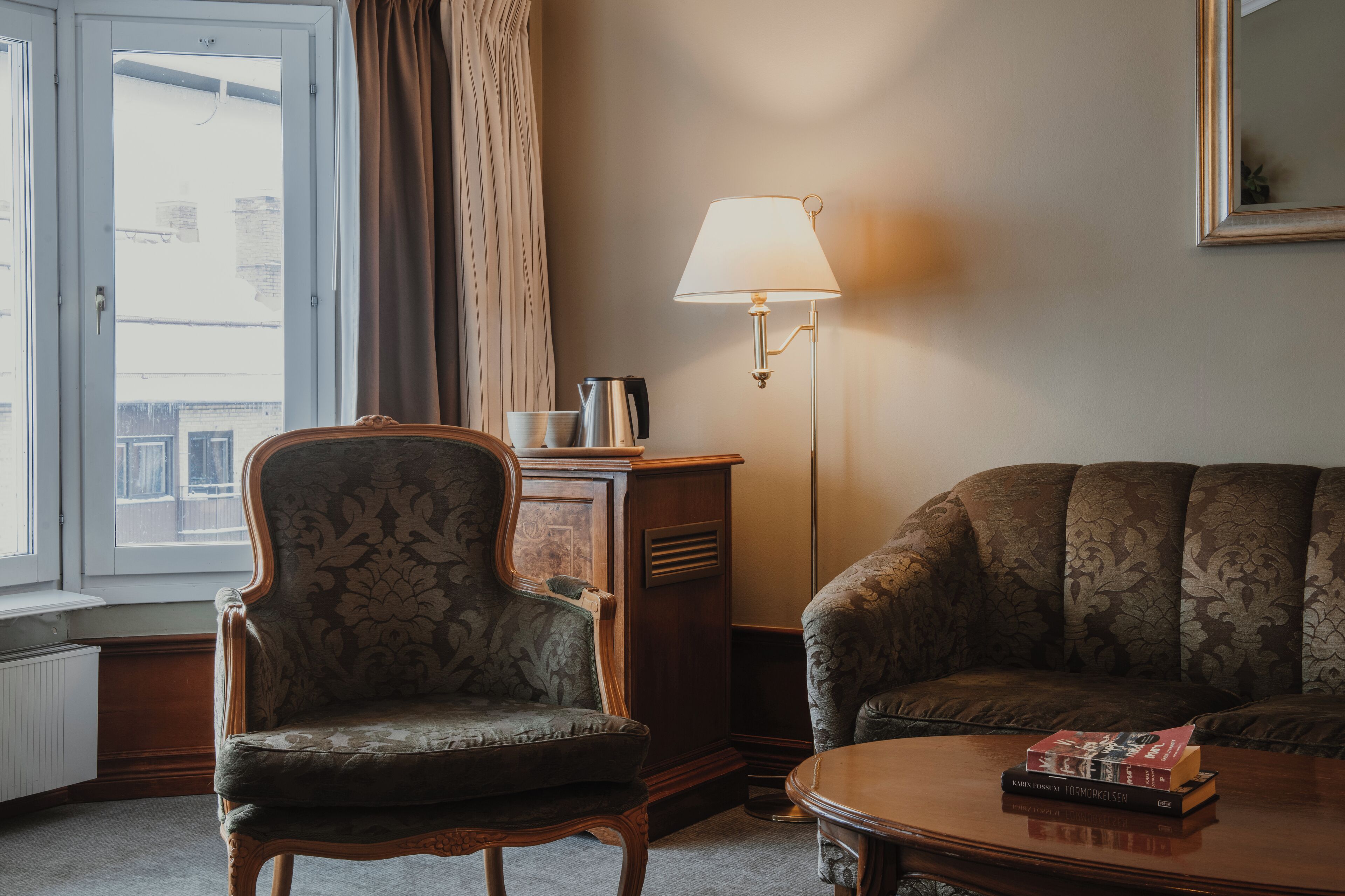 A room with a vintage armchair, a sofa, a lamp, and a coffee table with books.
