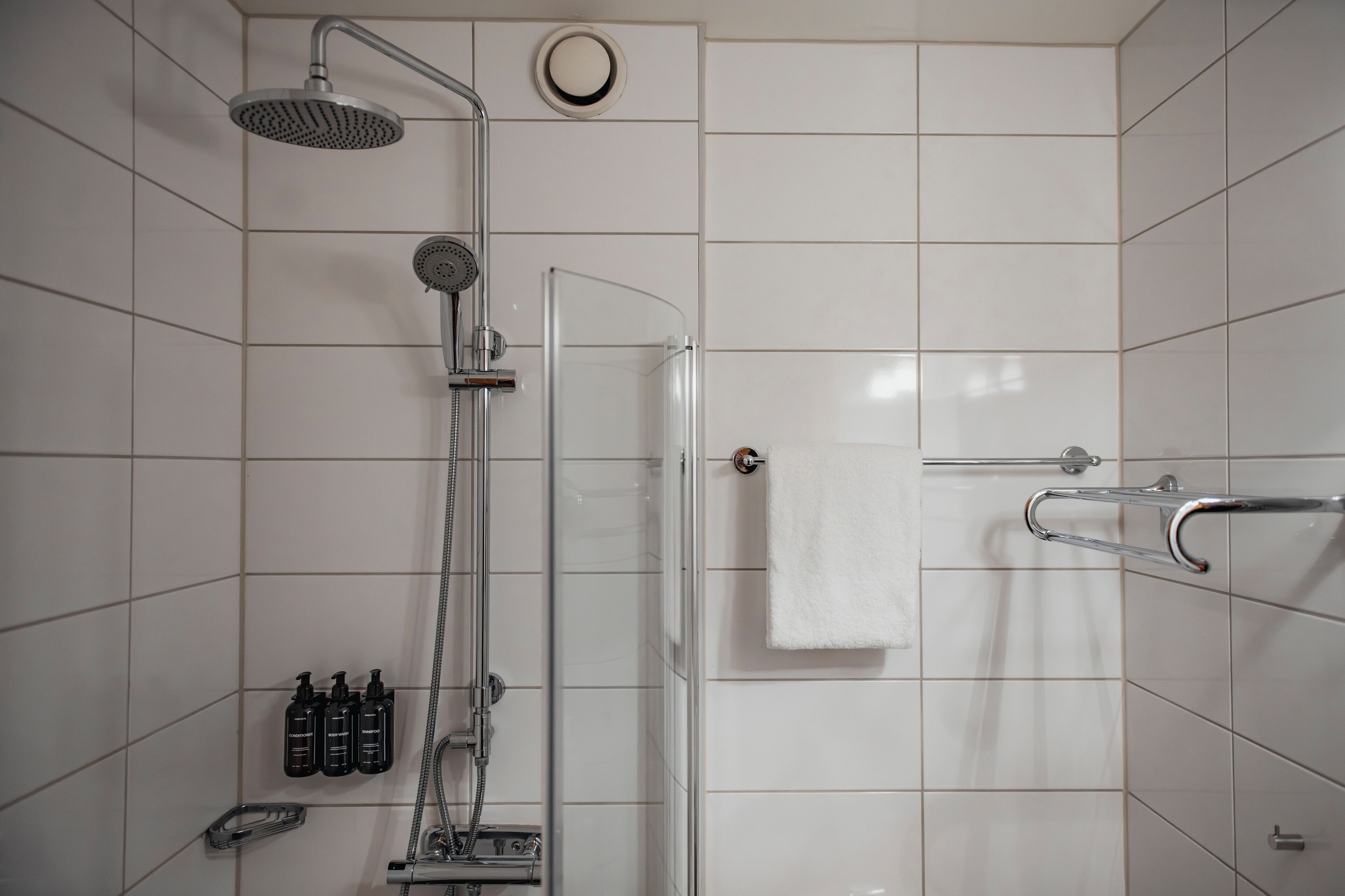 A modern shower area with a glass door, a handheld showerhead, a fixed showerhead, and a towel rack.