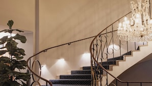 Eine Treppe mit einem schwarz-weißen Punkte-Teppich, einem großen Topf mit Pflanze und einer Kronleuchter.