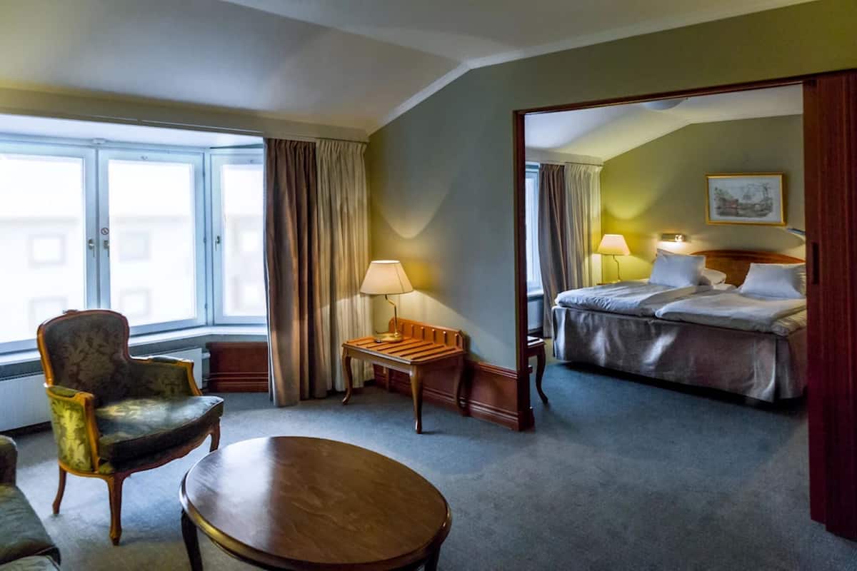 A hotel room with a bed, a chair, a table, and a window with curtains.