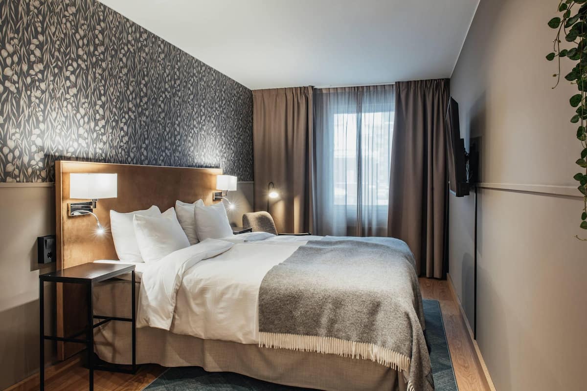 A hotel room with a bed, bedside tables, a TV, and a patterned wall.