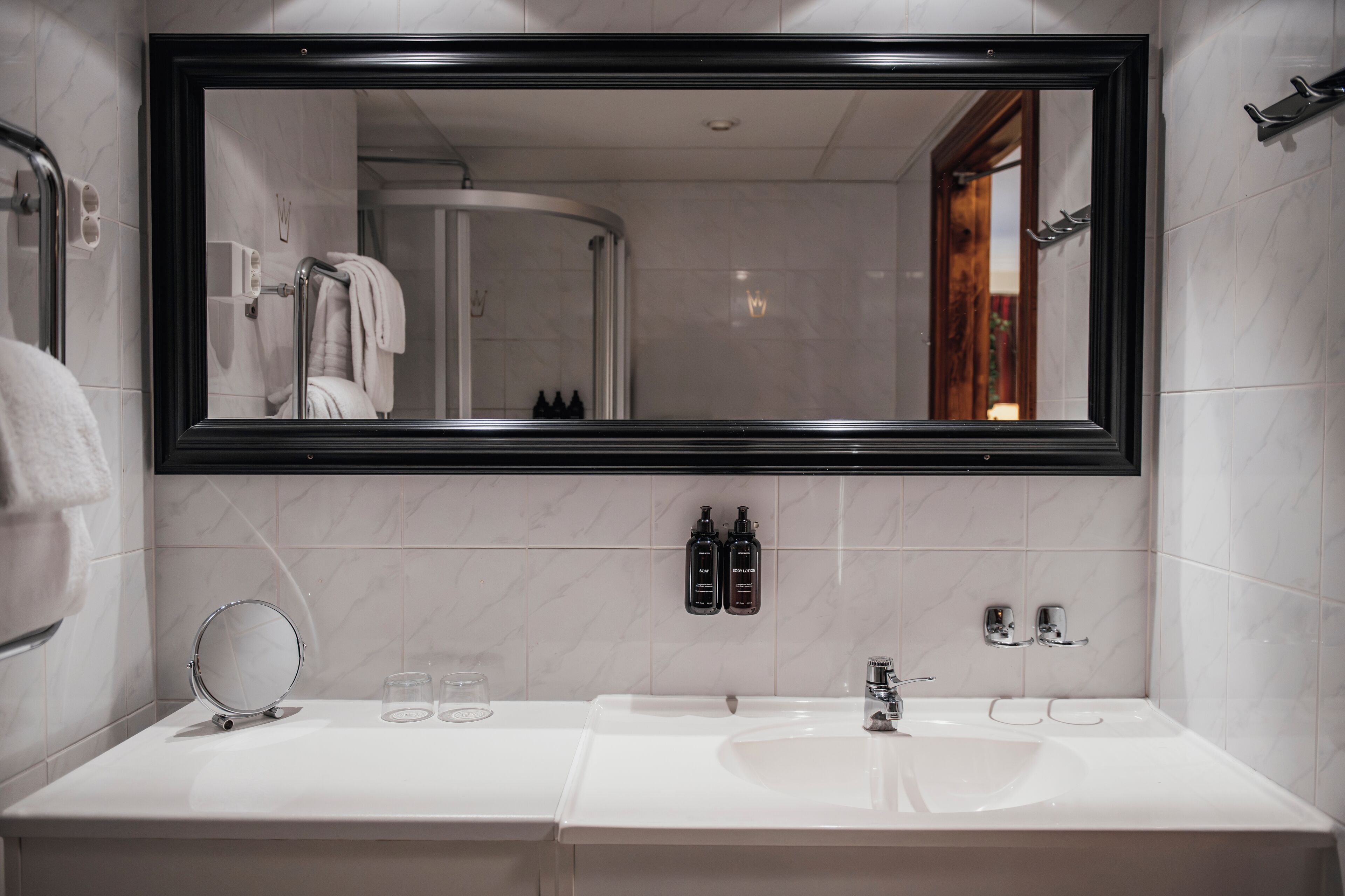 Een moderne badkamer met een grote spiegel, twee wasbakken, een ronde spiegel en toiletartikelen aan de muur.
