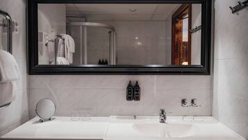 Een moderne badkamer met een grote spiegel, twee wasbakken, een ronde spiegel en toiletartikelen aan de muur.