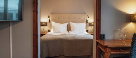 A hotel room with a large bed, bedside lamps, a TV, a wooden desk, and a chair.