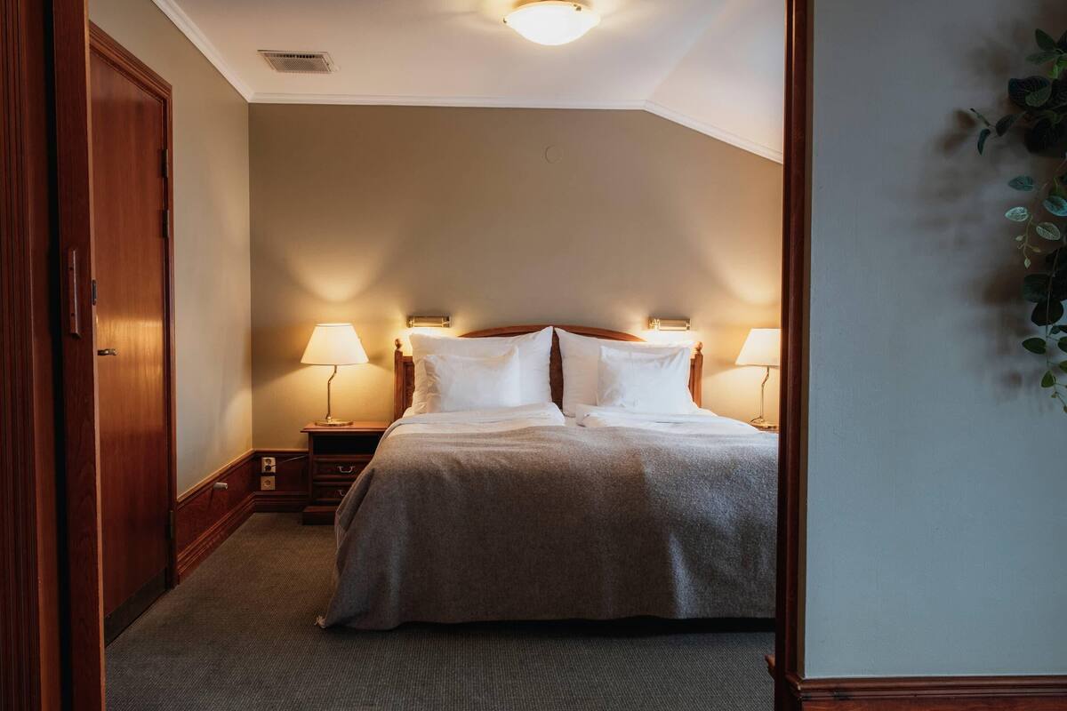 A hotel room with a bed, two bedside lamps, a nightstand, and a door.