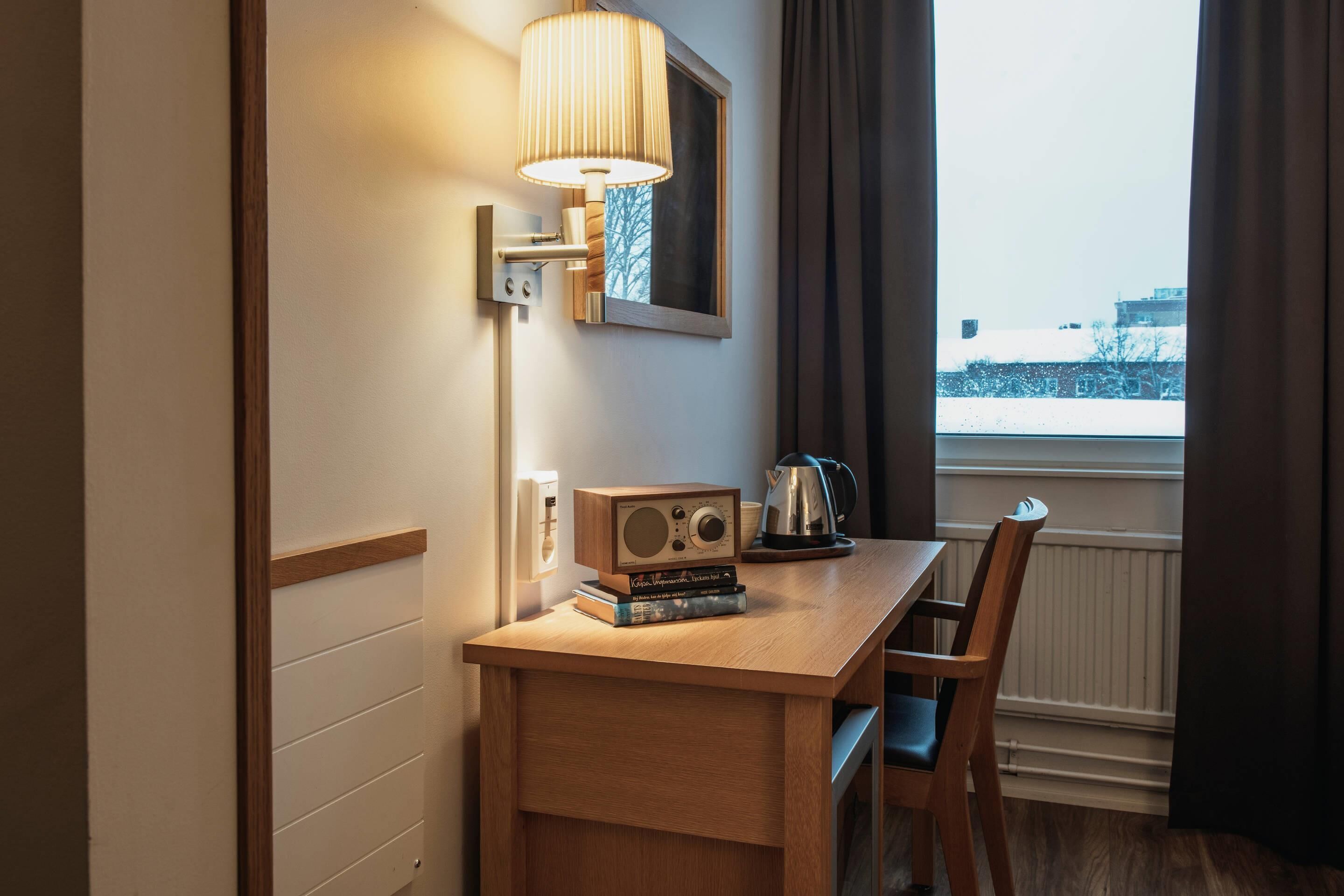A hotel room with a wooden desk, a radio, a kettle, and a view of a snowy landscape.