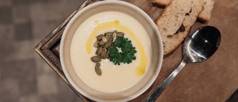 A bowl of creamy soup garnished with seeds and parsley, accompanied by slices of bread and a spoon on a wooden tray.