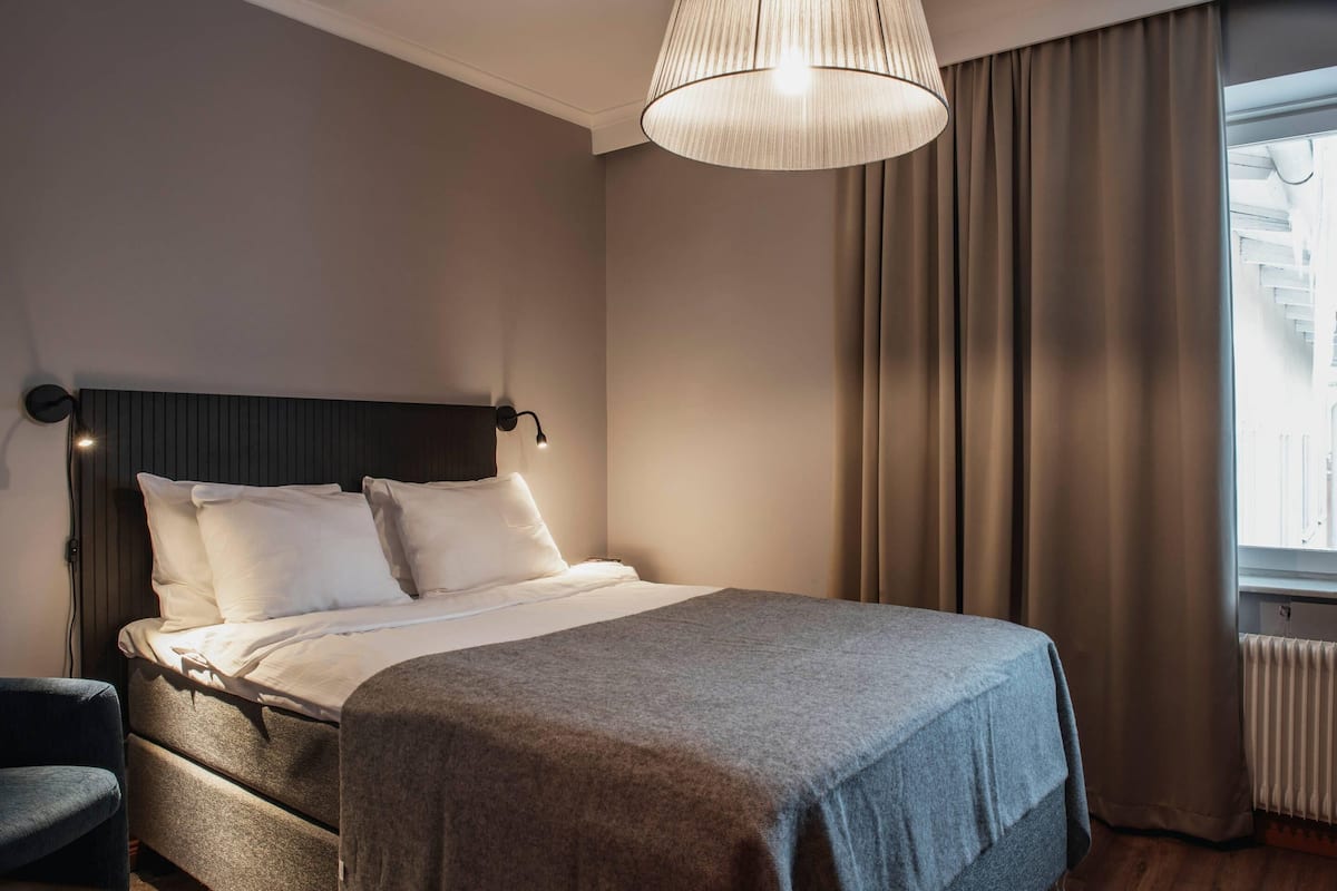 A hotel room with a bed, a chair, a lamp, and a window with curtains.
