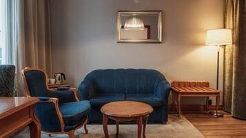 Ein Zimmer mit einem blauen Sofa, einem Holztisch, einem Nachttisch, einem Sessel, einer Lampe und einem gerahmten Spiegel an der Wand.