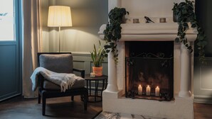 Ein gemütliches Zimmer mit Kamin, einem Sessel, einem Tisch und einer Lampe.