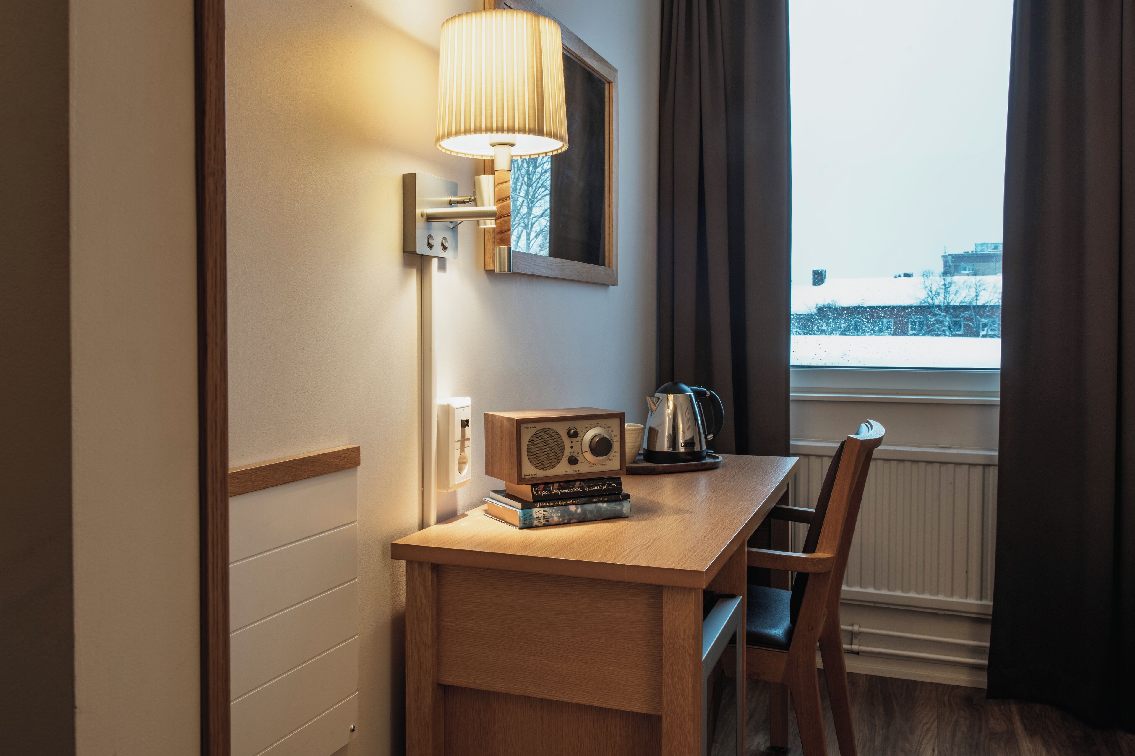 Ein Hotelzimmer mit einem Holztisch, einem Radio, einem Wasserkocher und Blick auf eine verschneite Landschaft durch ein Fenster.