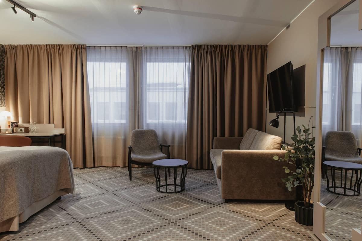 A hotel room with a bed, two armchairs, a sofa, a small table, a TV, and a potted plant.