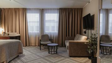A hotel room with a bed, two armchairs, a sofa, a small table, a TV, and a potted plant.
