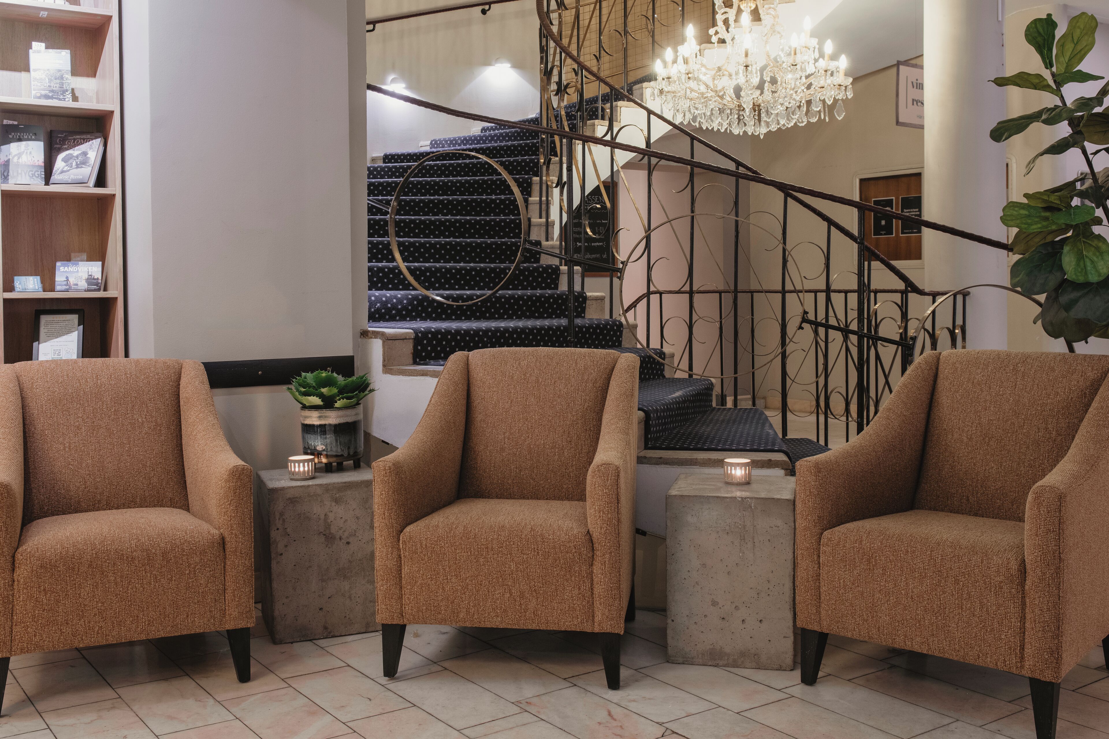 Un interior moderno con una escalera, dos sillones, una mesita con una planta y un candelabro.