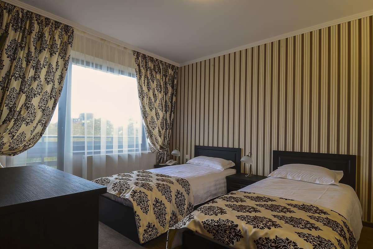 Een hotelkamer met twee bedden, een bureau en een groot raam met gordijnen.