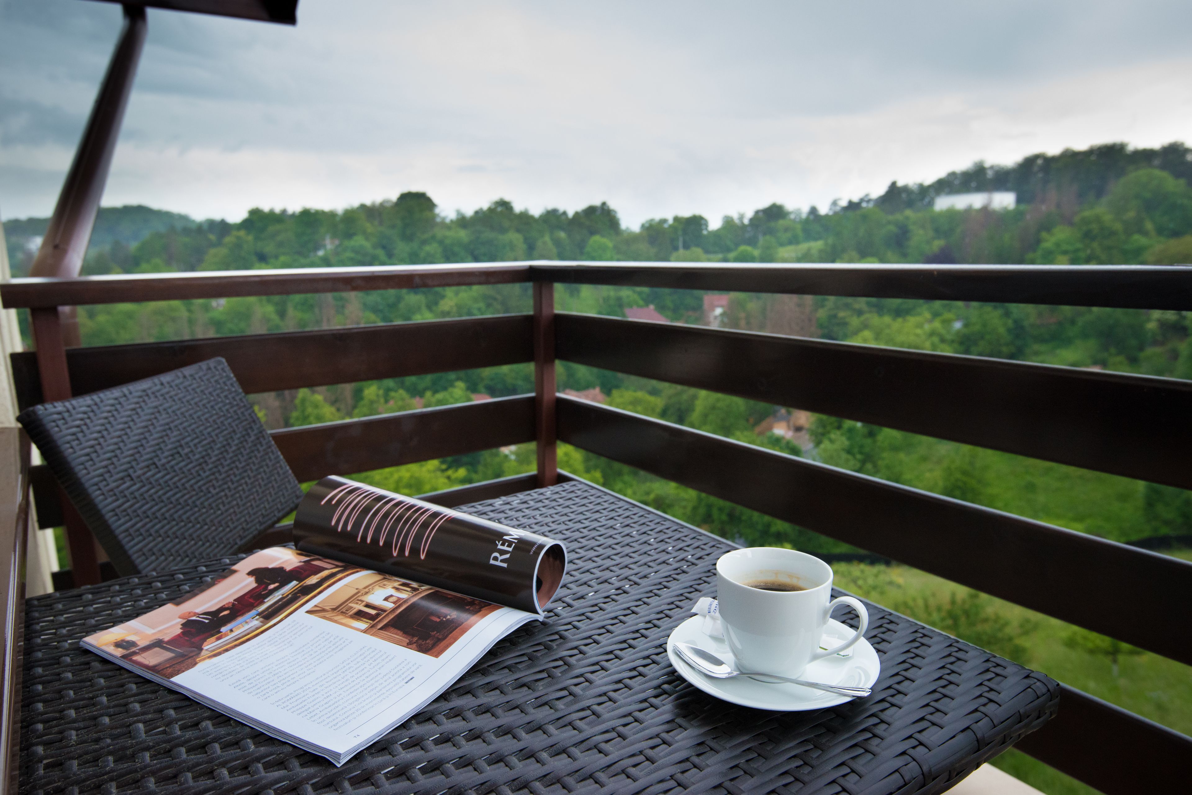 Un balcón con una mesa de mimbre, una taza blanca de café y una revista.