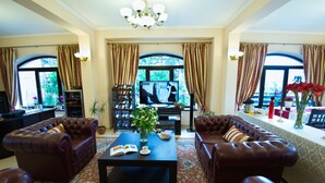 A spacious living room with two leather sofas, a coffee table, and a television. - Pensiunea Toscana (Brasov)