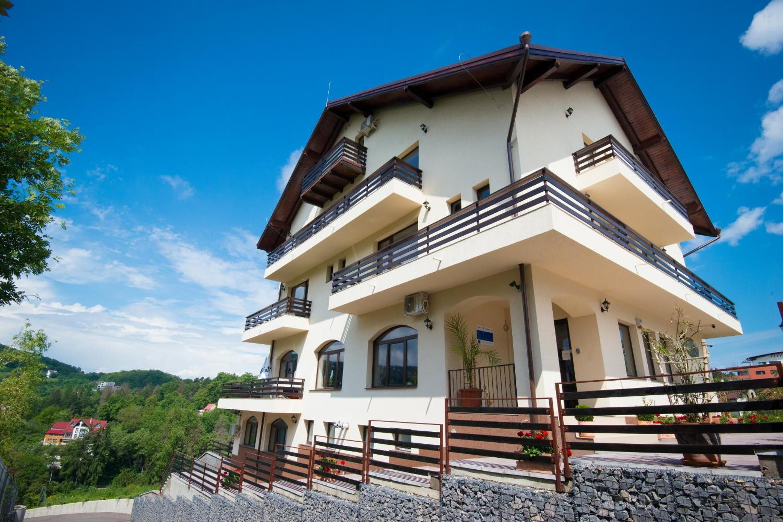 A multi-story building with balconies, a stone facade, and a clear view of the surrounding greenery.