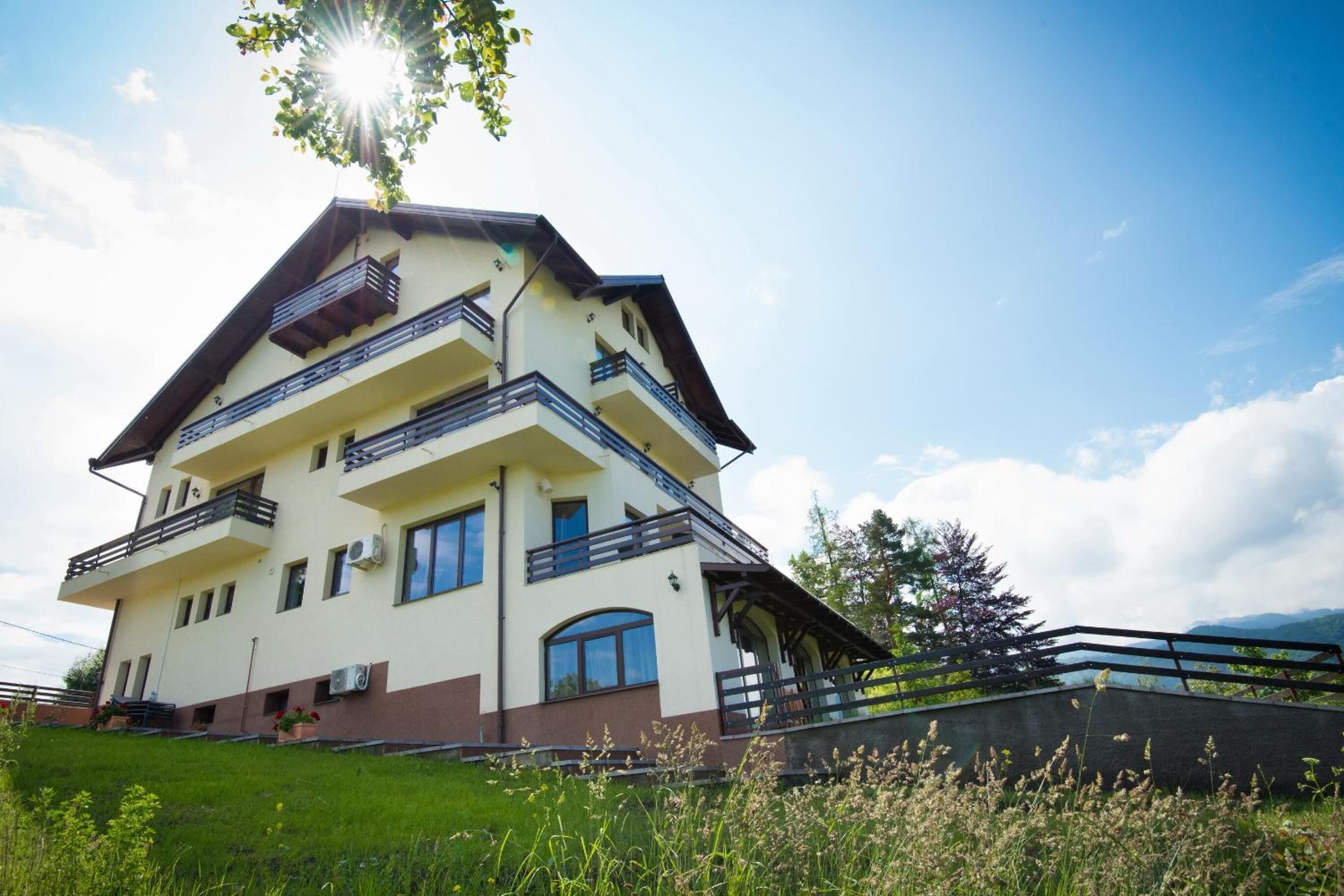 Un edificio a più piani con balconi, un tetto spiovente e vista sul paesaggio circostante.