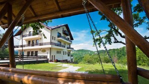 A wooden swing set overlooking a two-story building with balconies and a clear view of the surrounding greenery. - Pensiunea Toscana (Brasov)