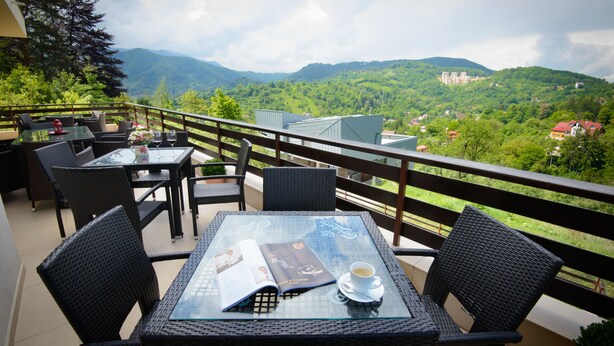 A balcony with wicker furniture, a glass table, and a magazine. - Pensiunea Toscana (Brasov)