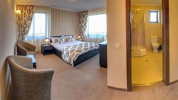 Camera d'albergo con un letto grande, due poltrone, un comodino, una doccia e un bagno.