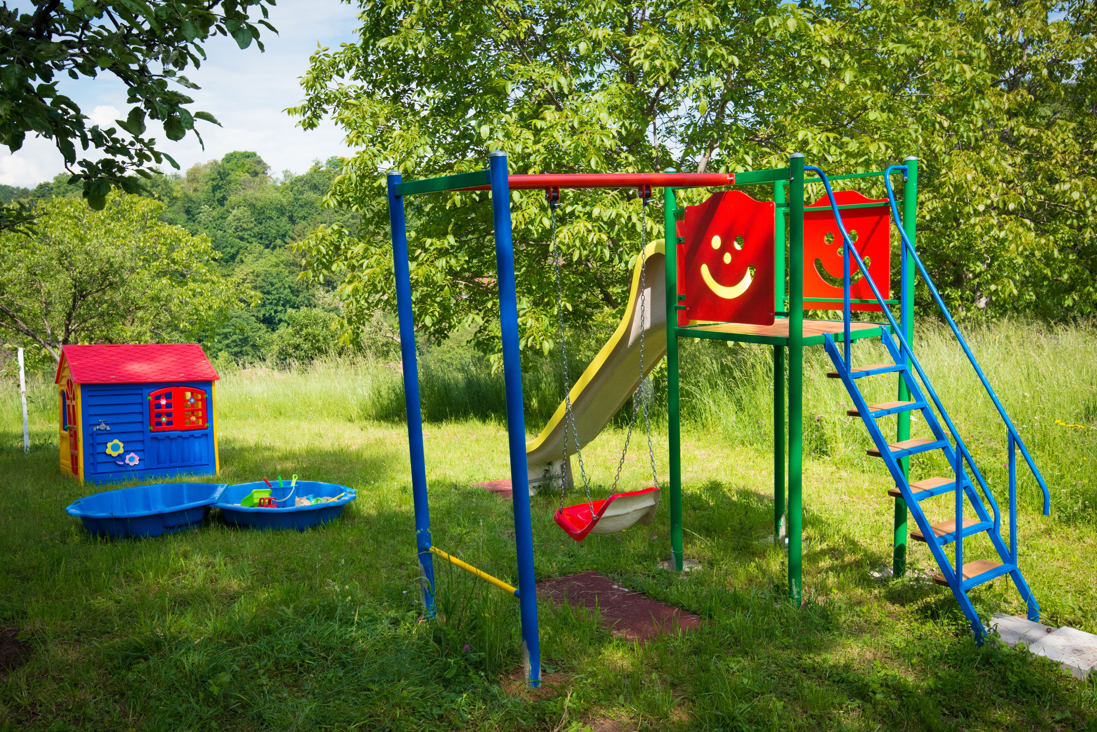 A playground with a slide, swings, and a small house.
