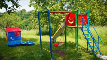 A playground with a slide, swings, and a small house.