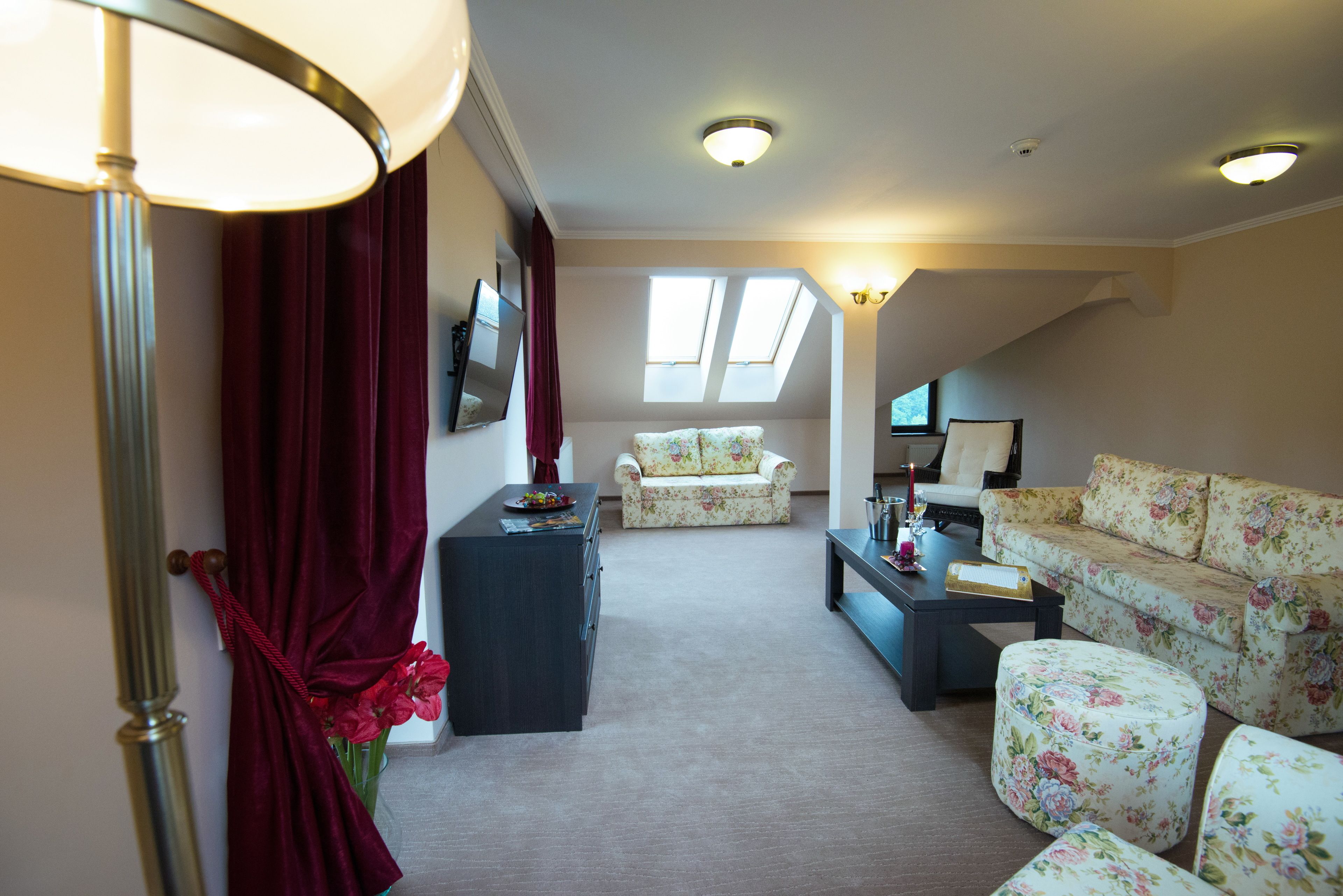 A living room with a sofa, a chair, a coffee table, and a lamp. There are windows and a ceiling light.