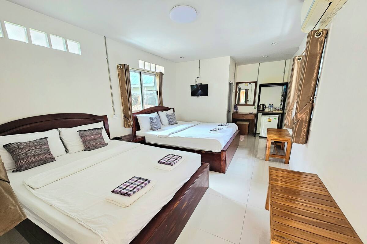 A hotel room with two beds, a wooden desk, a mirror, and a small kitchenette.