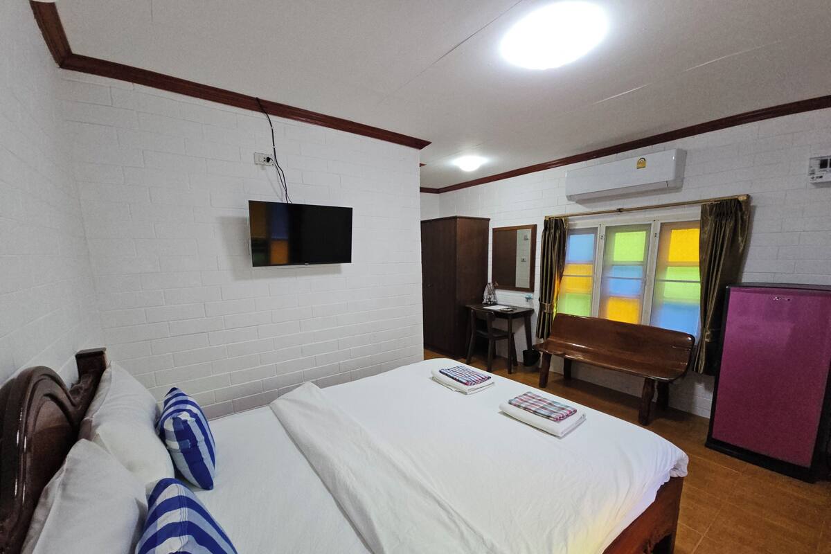 A hotel room with a bed, a desk, a chair, a TV, and a refrigerator.