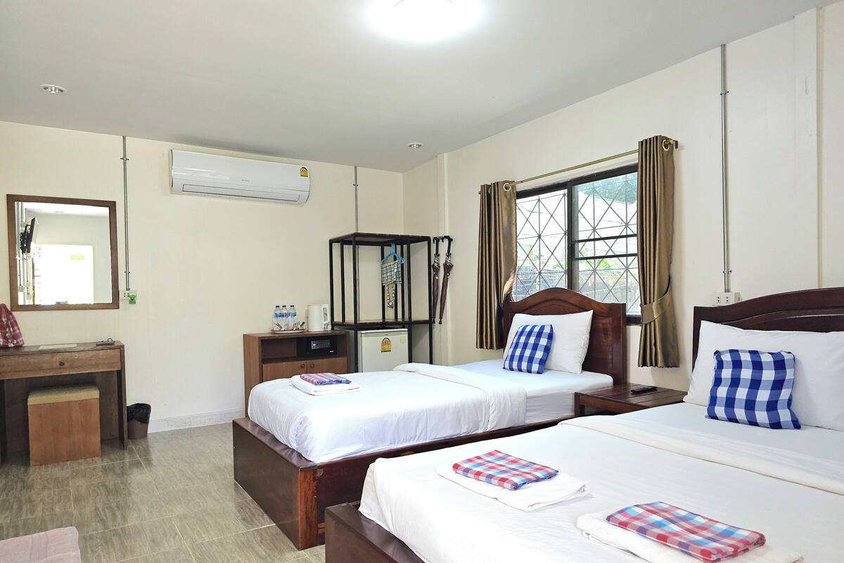 A hotel room with two beds, a desk, a small refrigerator, and a window with curtains.