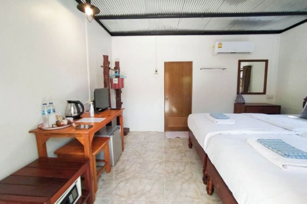 A room with a bed, a desk with a chair, a small table with a kettle, and a mirror on the wall.
