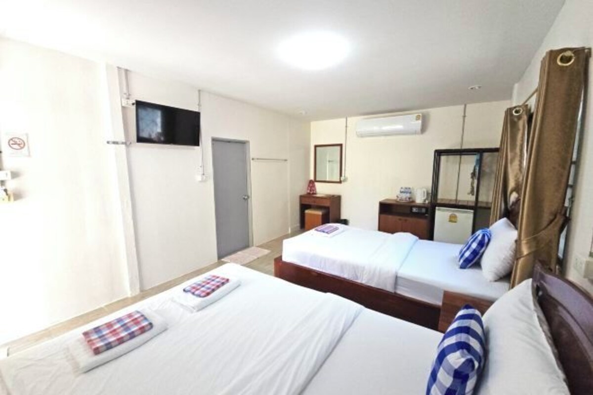 A hotel room with two beds, a television, an air conditioning unit, and a small desk with a mirror.