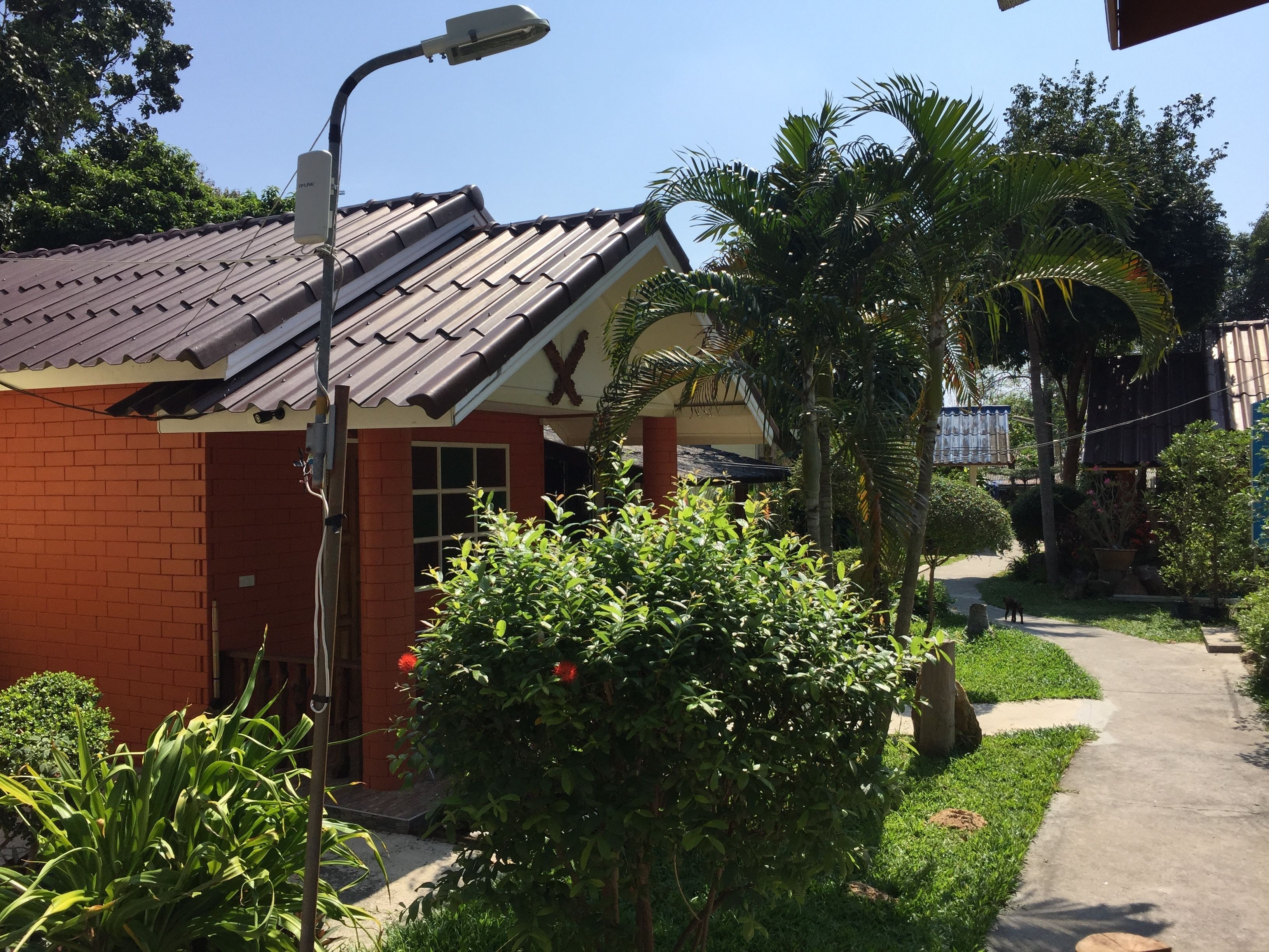 A small building with a tiled roof, a brick exterior, and a small porch. There is a street lamp and a sidewalk with a dog walking nearby.