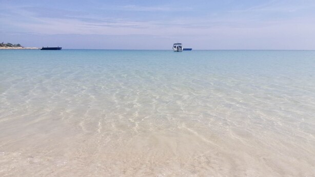 Ein Strand mit klarem, flachem Wasser und einem Boot in der Ferne.