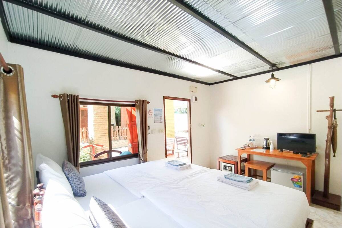 A hotel room with a bed, a desk with a television, a small table, and a window with curtains.