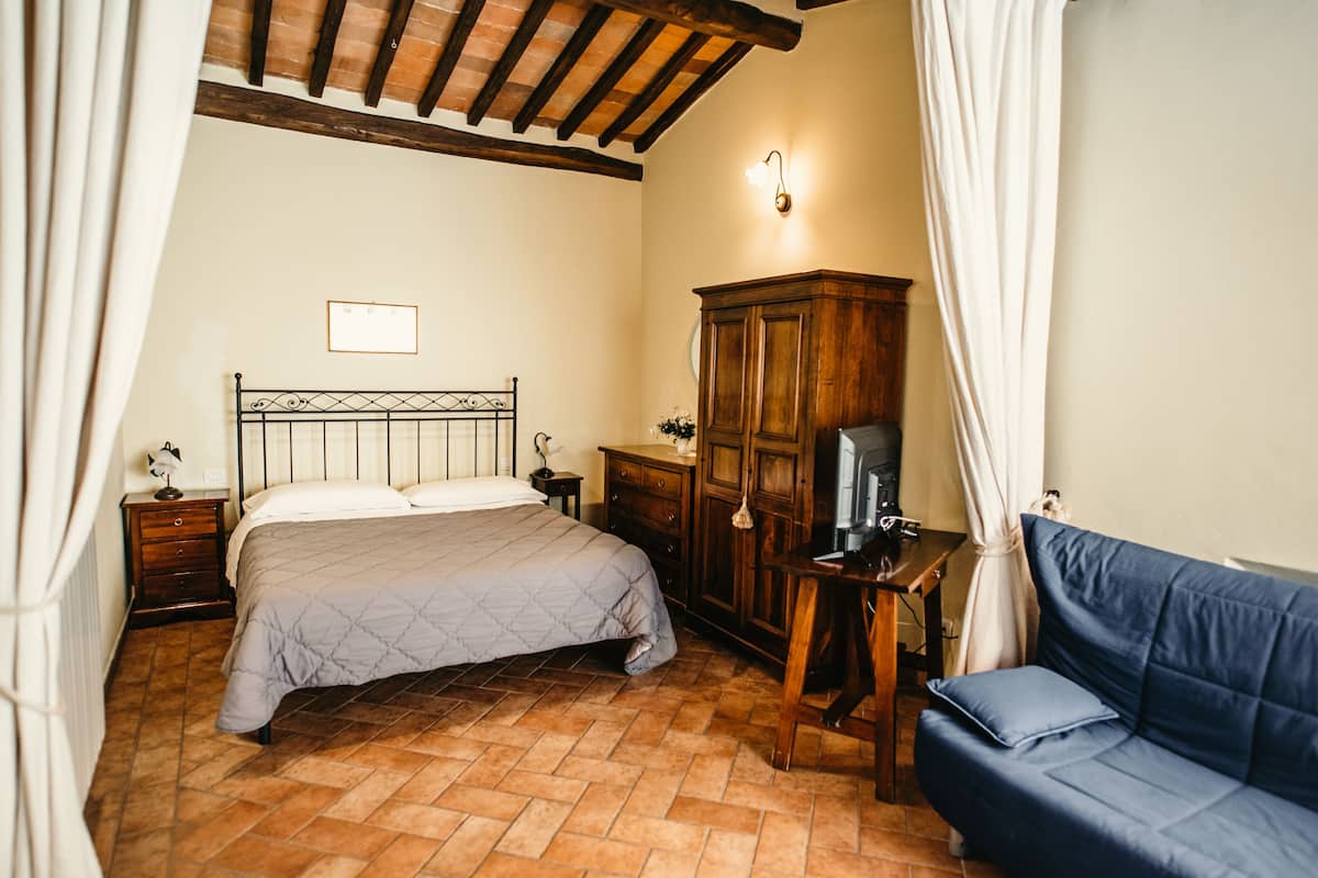 A bedroom with a bed, a wooden cabinet, a desk with a chair, and a blue sofa.