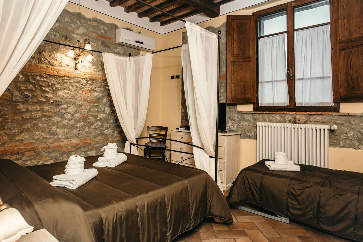 A room with two beds, a stone wall, a wooden cabinet, and a window with curtains.