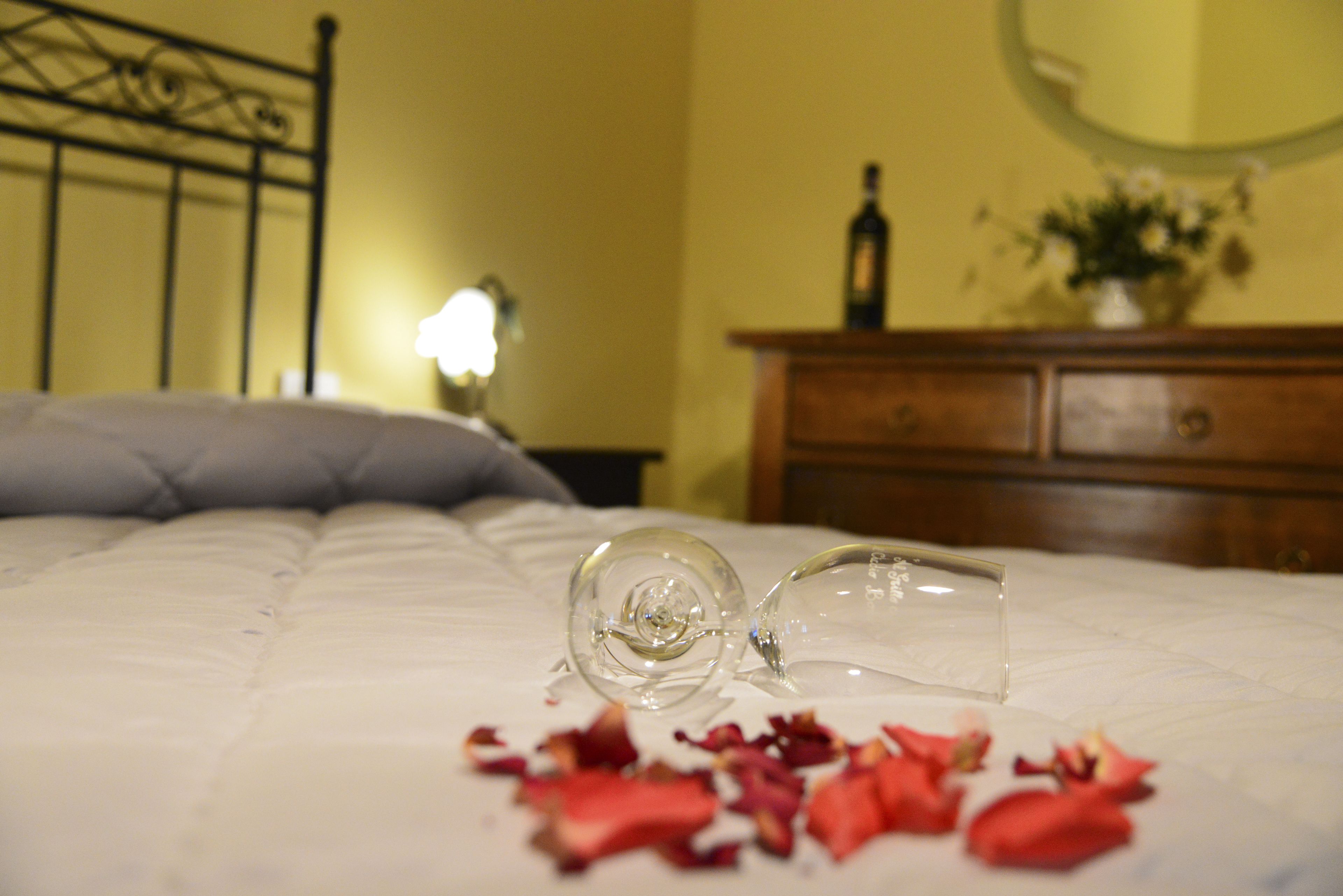 Una cama con una botella de vidrio transparente y pétalos de rosa.