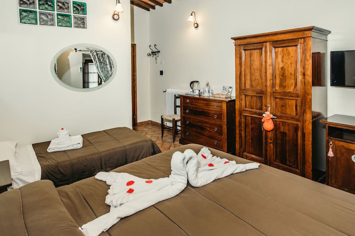 A hotel room with two beds, a wooden wardrobe, a mirror, and a radiator.