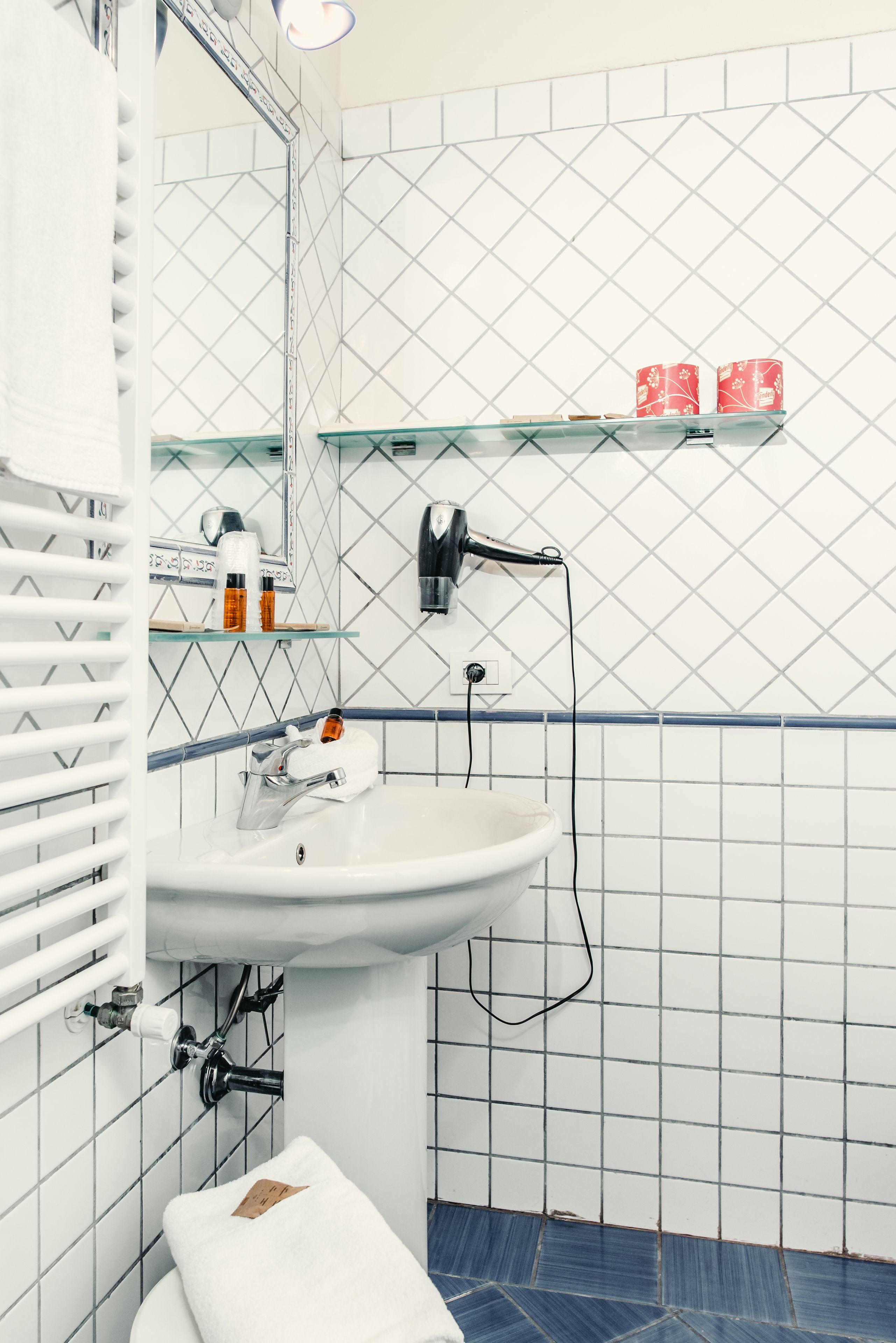 A bathroom with a white sink, a mirror, and a shelf with toiletries.