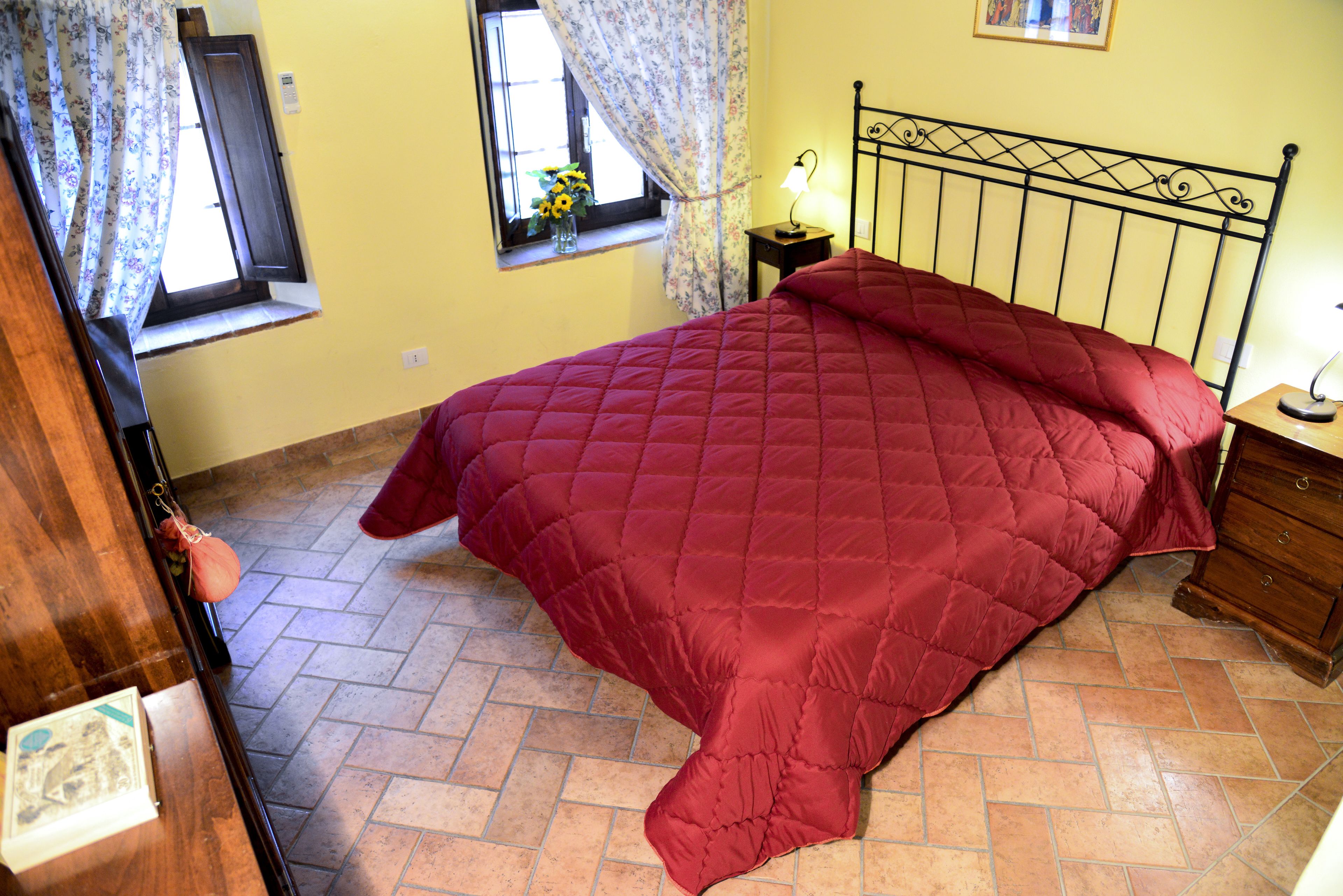 A room with a bed, a window with curtains, a bedside lamp, and a wooden dresser.
