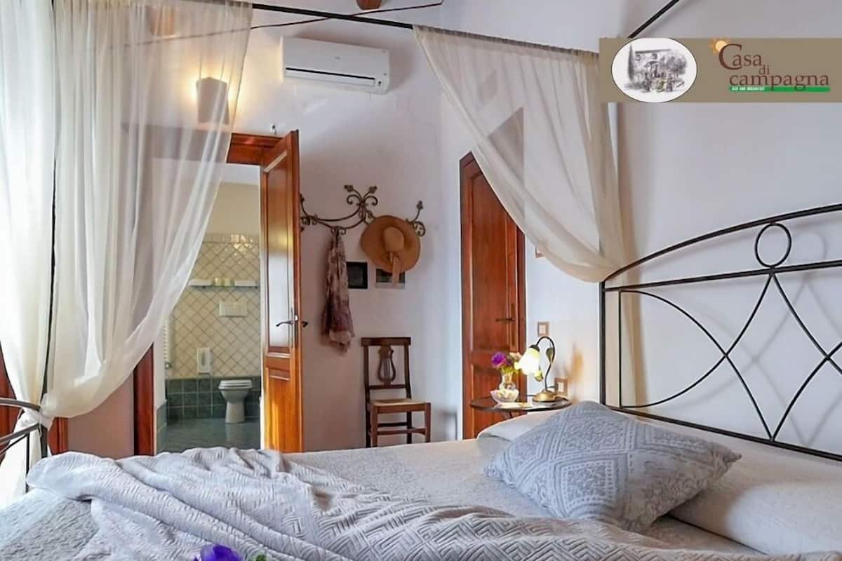 A bedroom with a bed, a bedside table with a lamp, a chair, and a wall-mounted air conditioner.