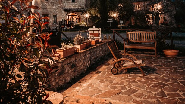 A stone courtyard with a bench, potted plants, and a building in the background. - Casa di Campagna in Toscana (Sovicille)