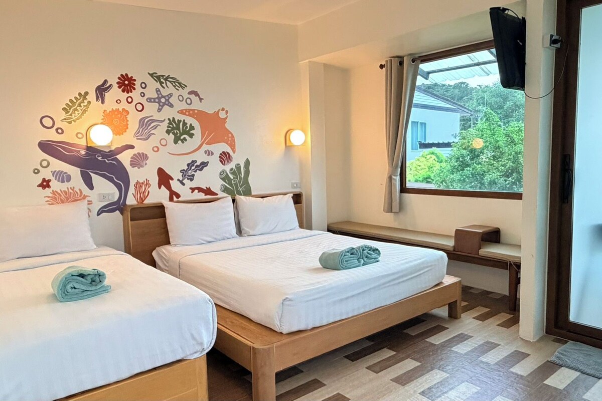 A hotel room with two beds, a wall mural, a window with a view, and a bedside table.