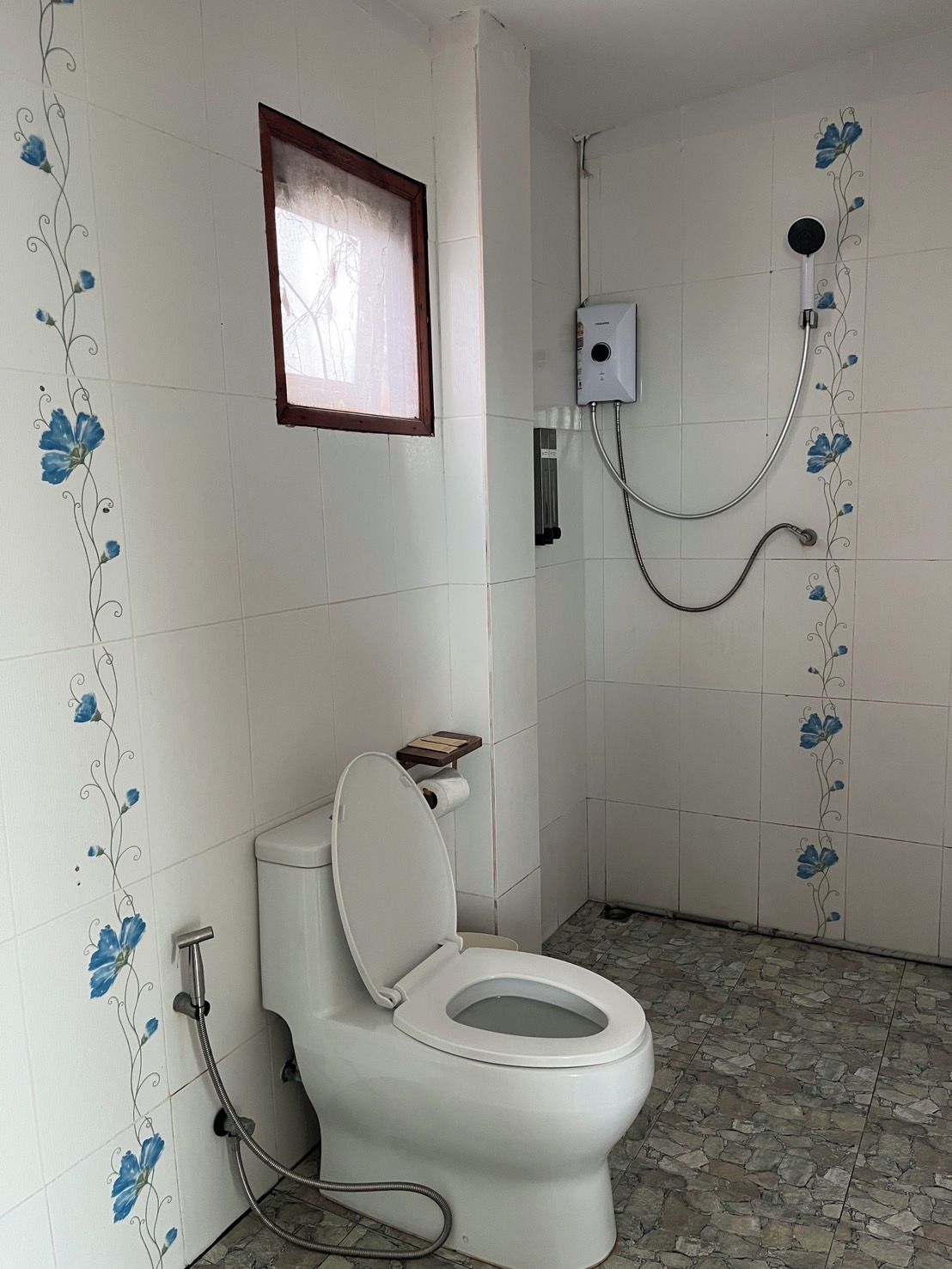 A bathroom with a toilet, shower, and a small window.