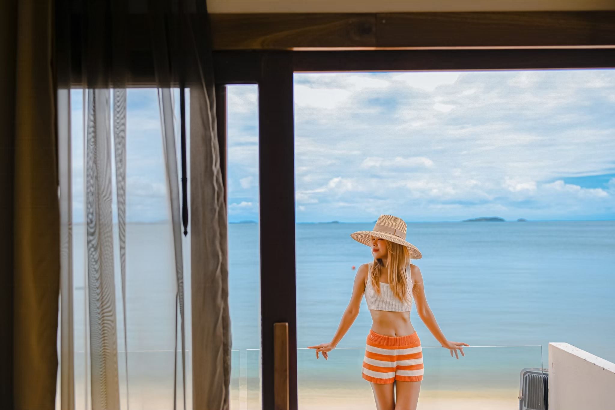 Una persona de pie junto a un ventanal con vista a la playa.